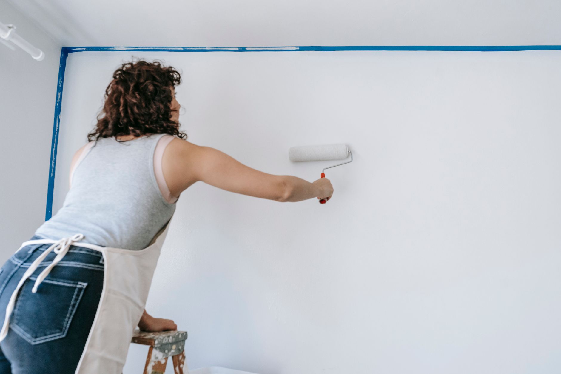 A woman stands on a ladder and paints a white wall during a home renovation project in Riverside, CA